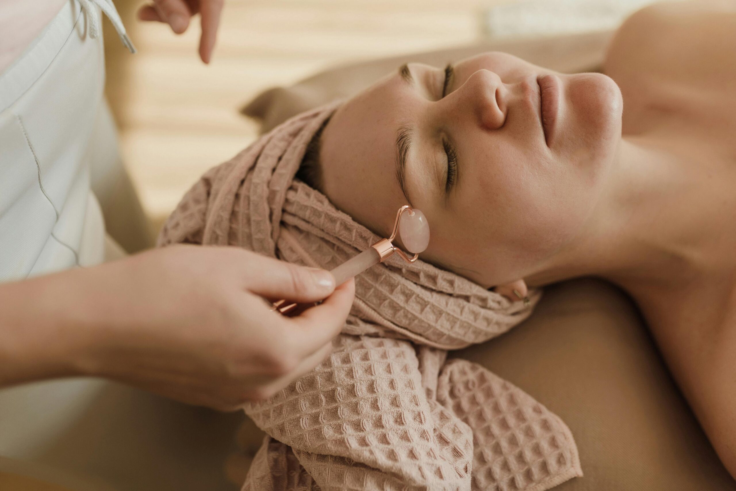 A woman with closed eyes enjoying a peaceful facial roller treatment in a spa setting.